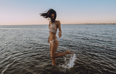 海滩上，一个穿比基尼的女孩在水里甩腿